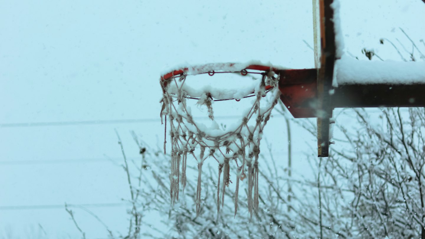 La neve copre il bordo rosso e la rete bianca di un canestro da basket.